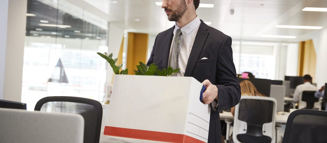 Fired male employee holding box of belongings in an office