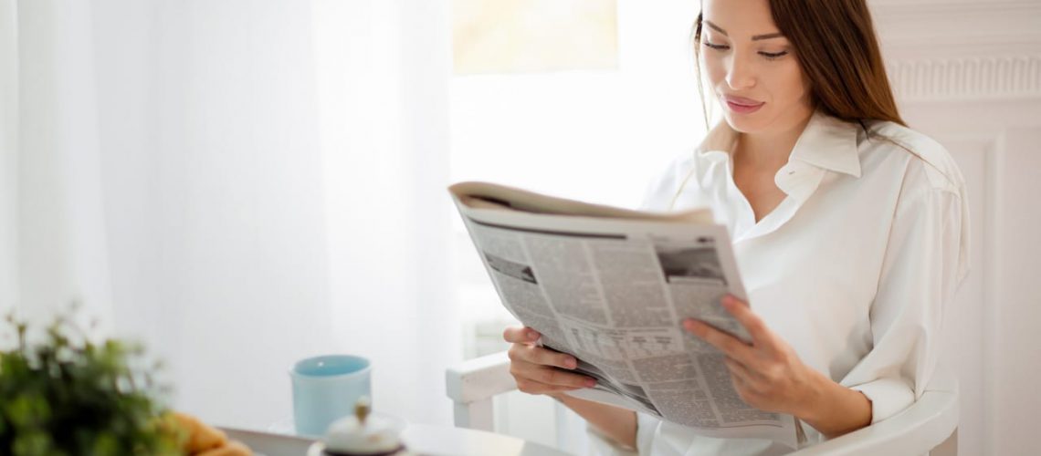 Young beautiful woman reading magazine at table in morning
