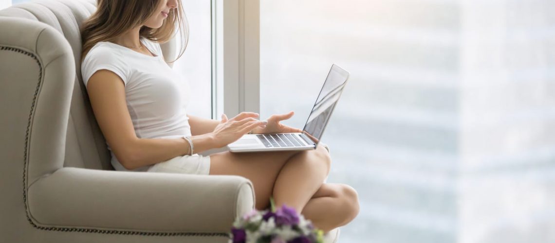 Young woman in a modern room, comfortable in her armchair with a laptop, operating her business, setting up business on the Internet, seeking for potential customers, SEO consultant. Lifestyle